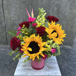 Bouquet of sunflowers, red roses, and pink flowers in a pink vase