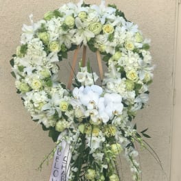 Large white floral funeral wreath on an easel with a ribbon