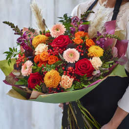 Large bouquet of red, orange, and pink flowers wrapped in paper