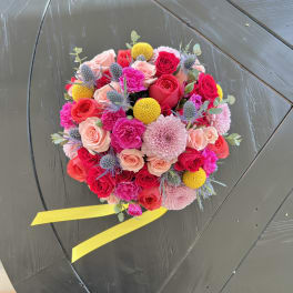 Round bouquet of pink and red roses with yellow accents and a yellow ribbon