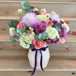 Pink and lavender bouquet in a white vase with a purple ribbon