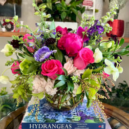 Mixed bouquet of pink roses, hydrangeas, and purple blooms in a glass vase