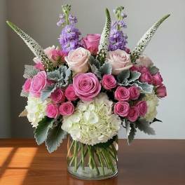 Pink and white rose bouquet with purple spikes in a glass vase