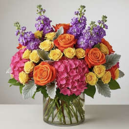 Bouquet of orange and yellow roses with pink and purple flowers in a glass vase