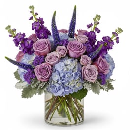 Lavender roses and blue hydrangeas in a clear glass vase