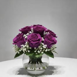 Purple roses arranged in a clear glass vase with white filler flowers