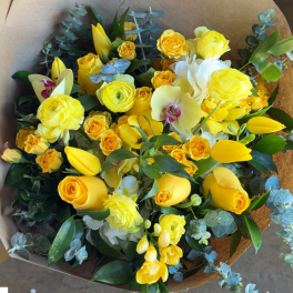 Yellow and white mixed bouquet with orchids and tulips wrapped in brown paper