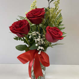 Three red roses in a clear glass vase with a red ribbon
