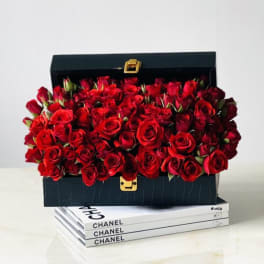 Black box filled with red roses on stacked Chanel books