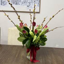Pink tulips and pussy willow branches in a glass vase with a red ribbon