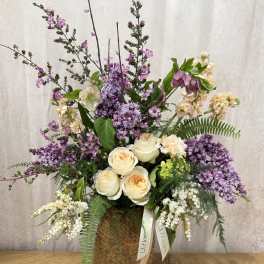 Tall floral arrangement with cream roses, purple blooms, and a woven basket vase