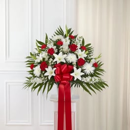 Standing floral spray of red roses and white lilies with a red ribbon
