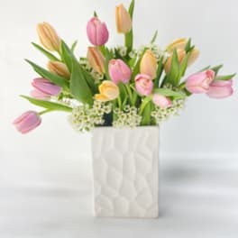 Pink and peach tulips arranged in a white textured vase