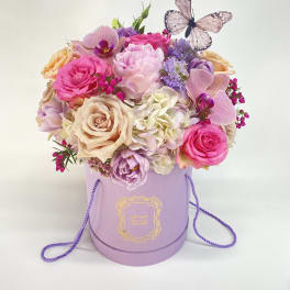 Pink and lavender flower arrangement in a lavender hat box with a butterfly topper