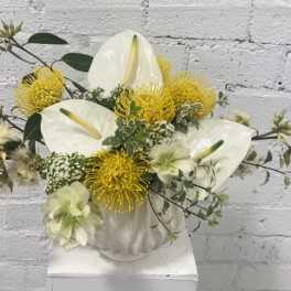 White anthuriums and yellow pincushion blooms in a white vase