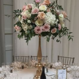 Tall floral centerpiece with pink and white roses on a gold stand