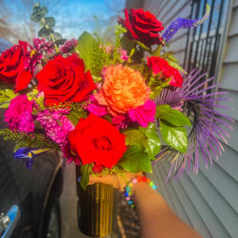 Bouquet of red and orange roses with purple accents in a gold vase