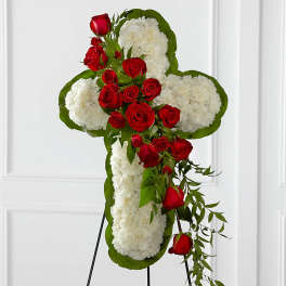 Cross-shaped floral tribute with red roses and white flowers on a stand
