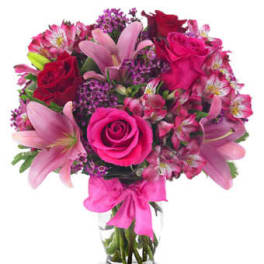 Pink lilies, roses, and alstroemeria arranged in a clear glass vase with a pink bow.