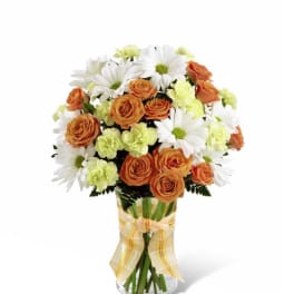 Vase arrangement with orange roses, white daisies, and pale green carnations with a yellow plaid bow.