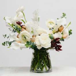 White floral arrangement in a clear glass vase with calla lilies and ranunculus