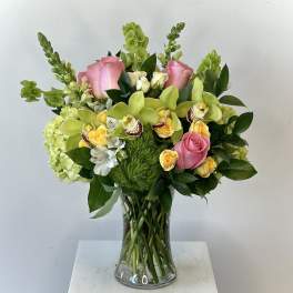 Bouquet of pink roses, green orchids, and yellow flowers in a glass vase