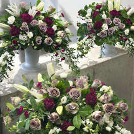 Three floral arrangements in white pedestal vases with roses and lilies