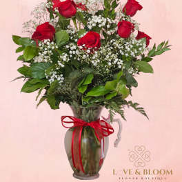 Red roses arranged in a glass pitcher with baby's breath and greenery