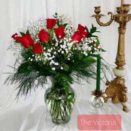Red roses and baby's breath in a clear glass vase beside a gold candlestick