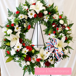 Large floral wreath with white lilies, daisies, and red roses on a stand