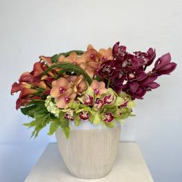 Mixed orchid arrangement in a light wood vase