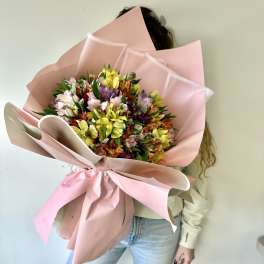 Person holding a large bouquet of multicolored flowers wrapped in pink paper