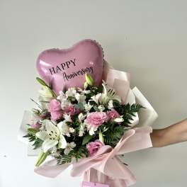 Pink anniversary balloon above a bouquet of white lilies and pink flowers