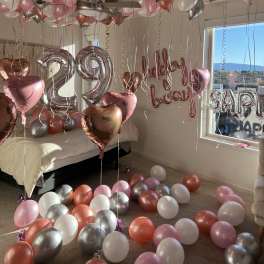 Pink, silver, and white balloons fill a decorated bedroom with "happy birthday" and "29" balloons.