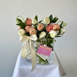 Bouquet of pink and white ranunculus in a glass vase with a ribbon