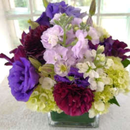 Purple, white, and green floral arrangement in a square glass vase