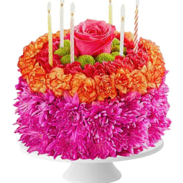 Flower cake with pink roses, orange carnations, and striped candles on a white stand