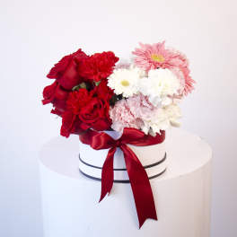 Round box of red, pink, and white flowers tied with a red ribbon