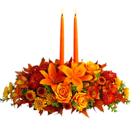 Orange floral centerpiece with two lit taper candles