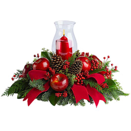 Red candle in a glass hurricane surrounded by apples, pinecones, and ribbon