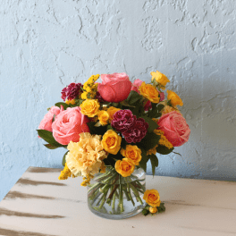 Mixed bouquet of pink, yellow, and burgundy flowers in a clear glass vase
