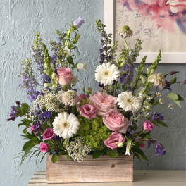 Mixed pink, white, and purple flowers arranged in a wooden box