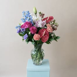 Colorful bouquet in a clear glass vase with roses, lilies, and anthuriums