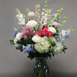 Mixed bouquet of roses, hydrangeas, and blue flowers in a glass vase