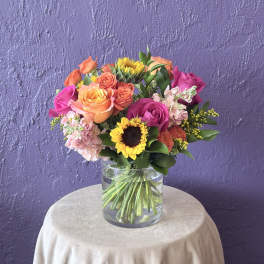 Mixed bouquet of roses, sunflowers, and pink blooms in a clear glass vase