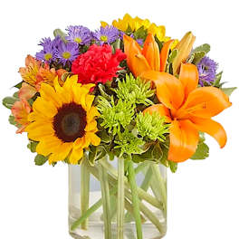 Mixed bouquet of sunflowers, lilies, and purple daisies in a glass vase