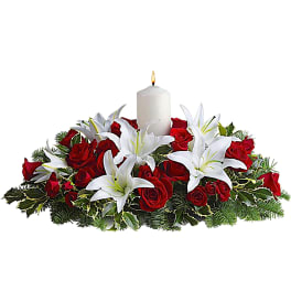 Red roses and white lilies arranged around a lit white candle