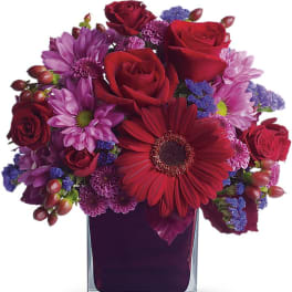 Red and purple mixed bouquet with roses and gerbera daisies in a square glass vase