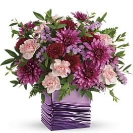 Short arrangement of pink carnations and purple chrysanthemums in a shiny purple square vase