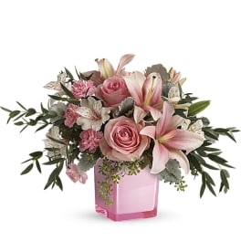 Low pink arrangement with lilies, roses, carnations, and alstroemeria in a pink glass cube vase